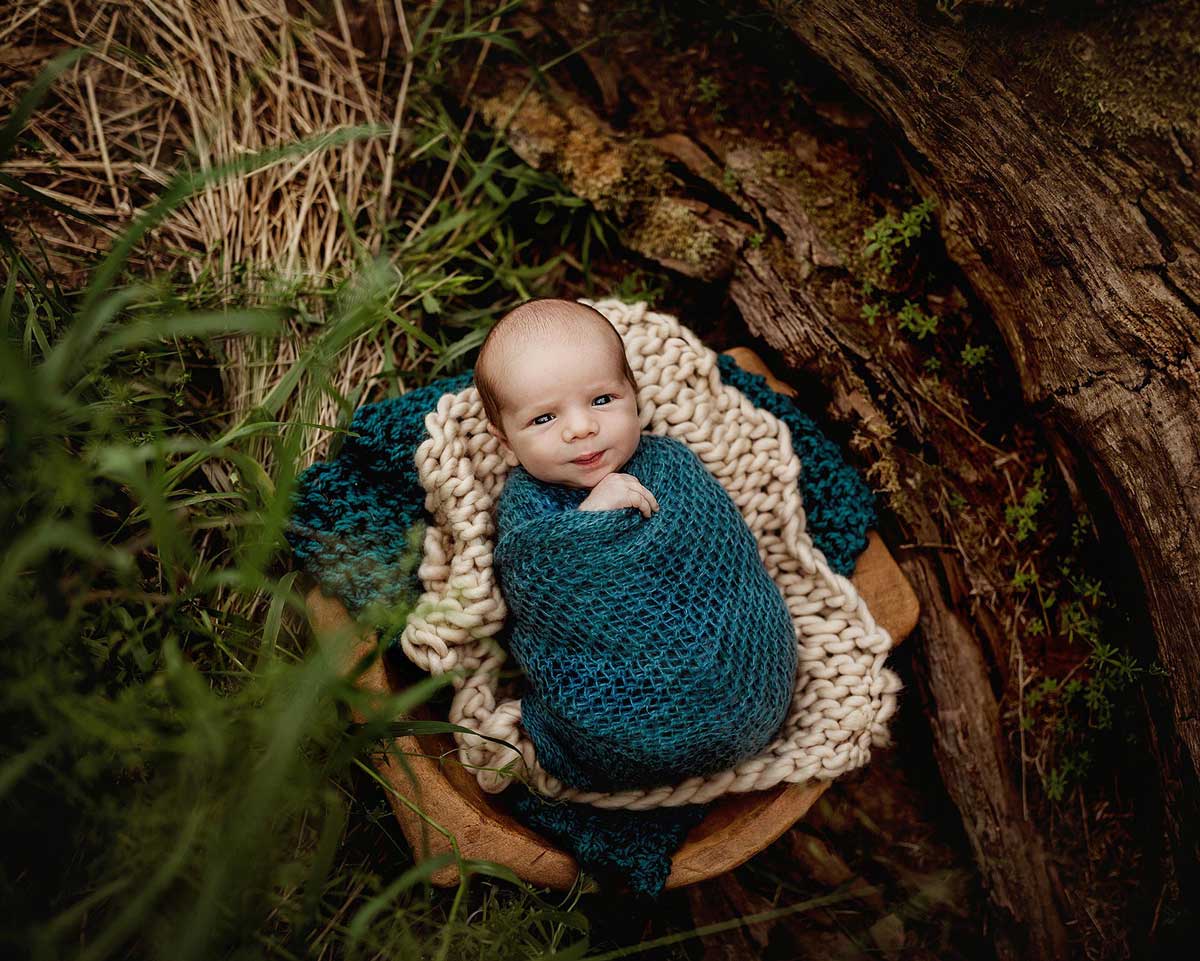 baby outdoors in wood bowl from newborn session